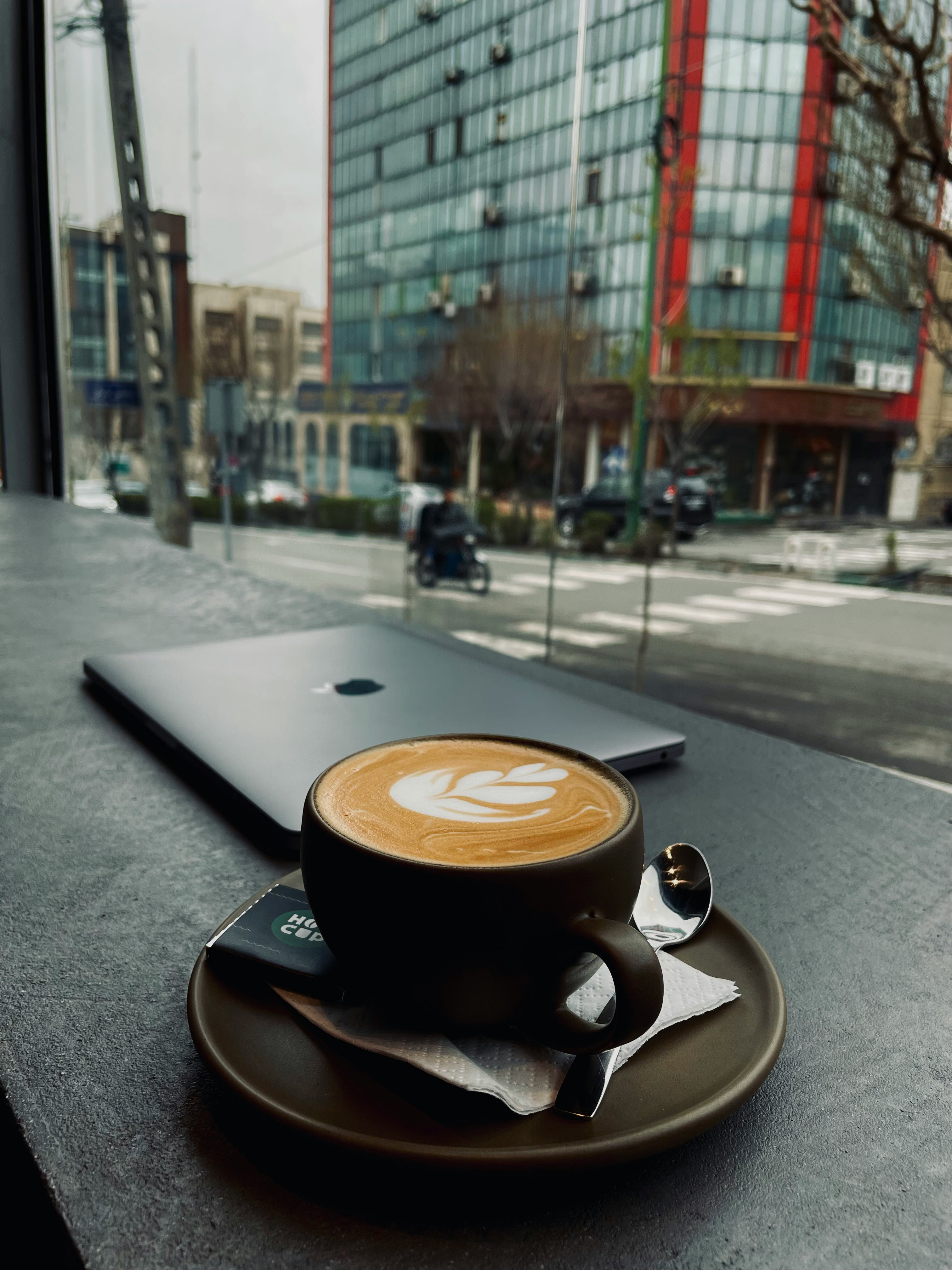 Cafe latte art beside a laptop with city view through the window