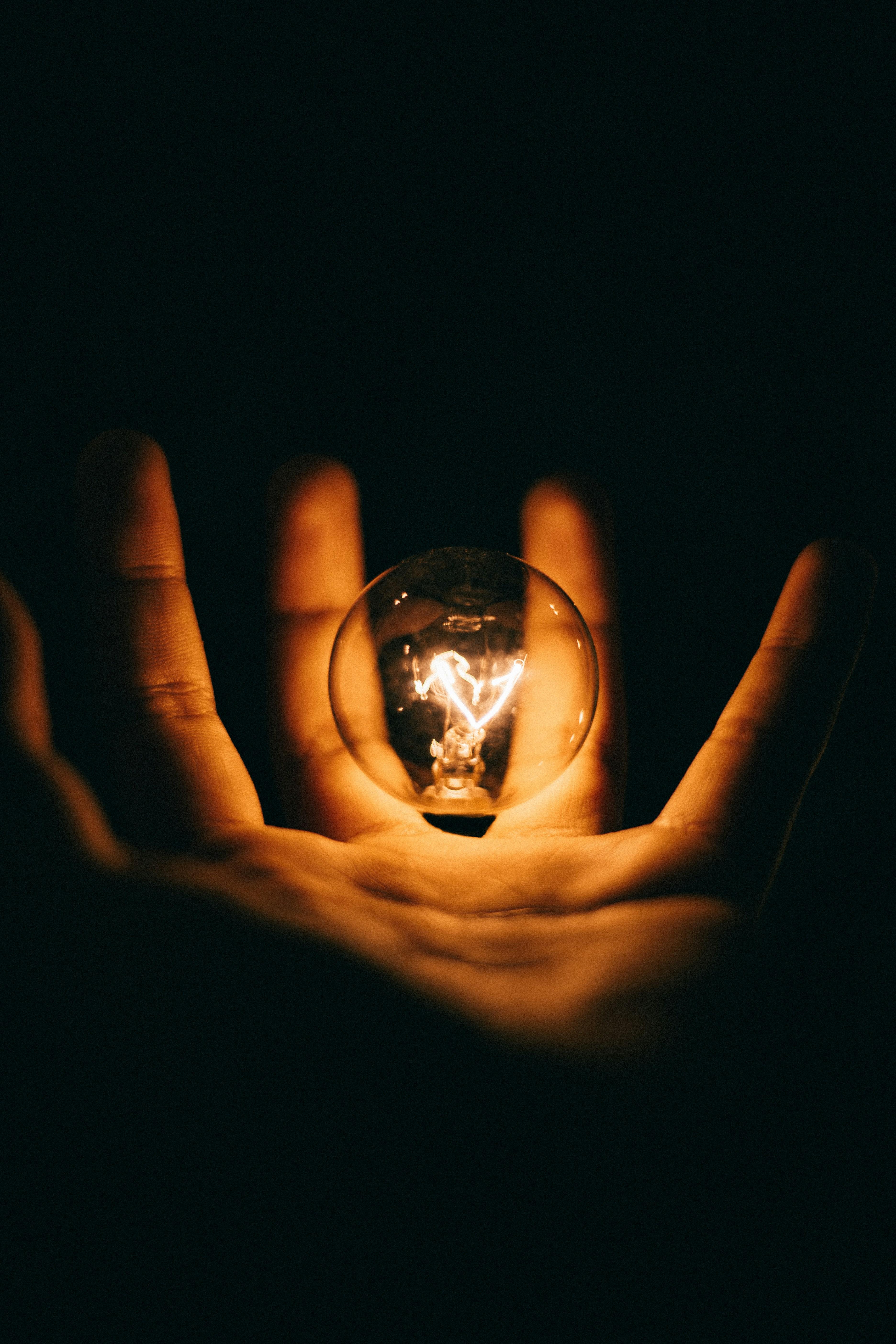 Glowing lightbulb held in cupped hands against dark background