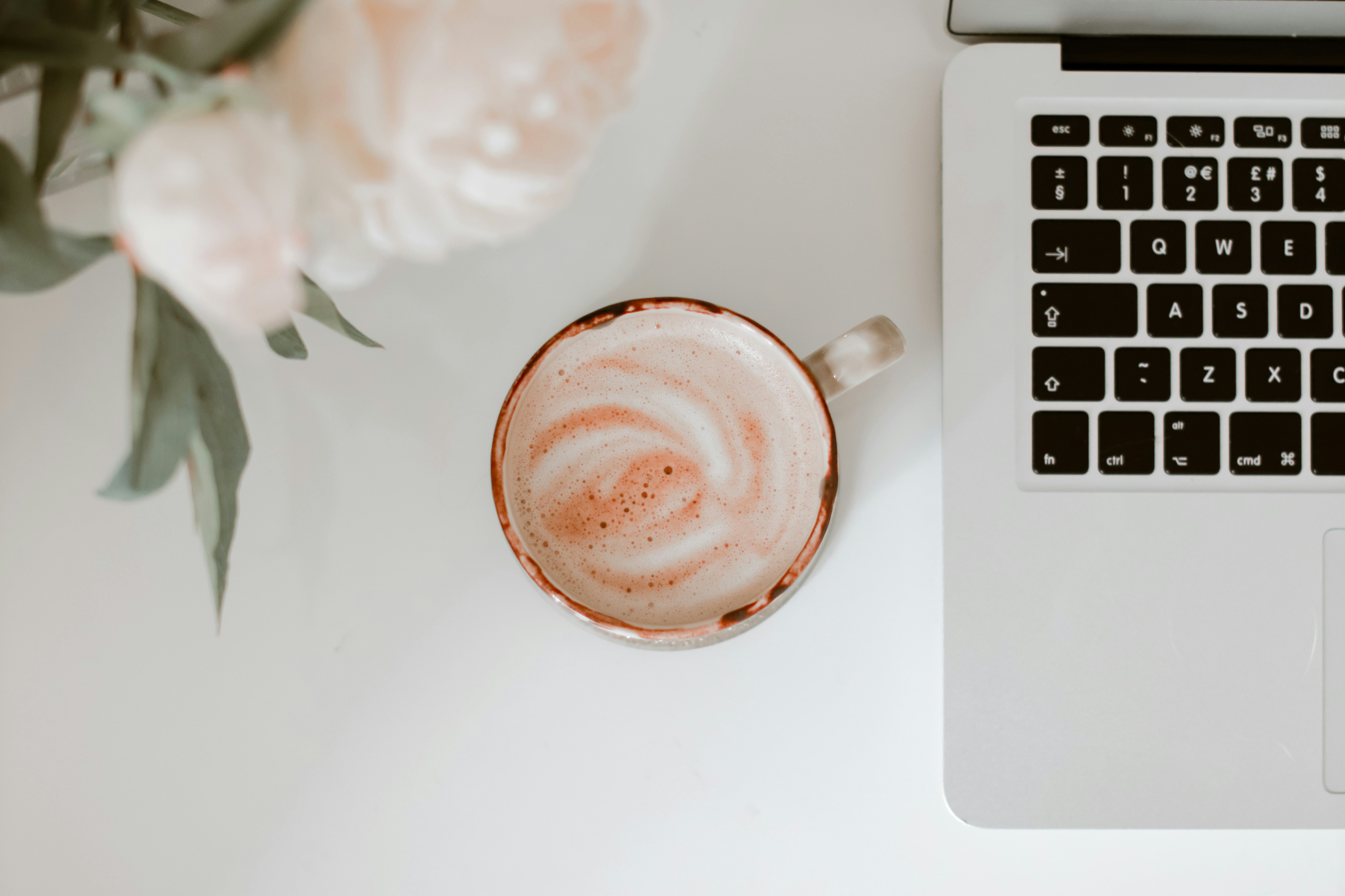 Latte flatlay with MacBook and peonies on a white desk