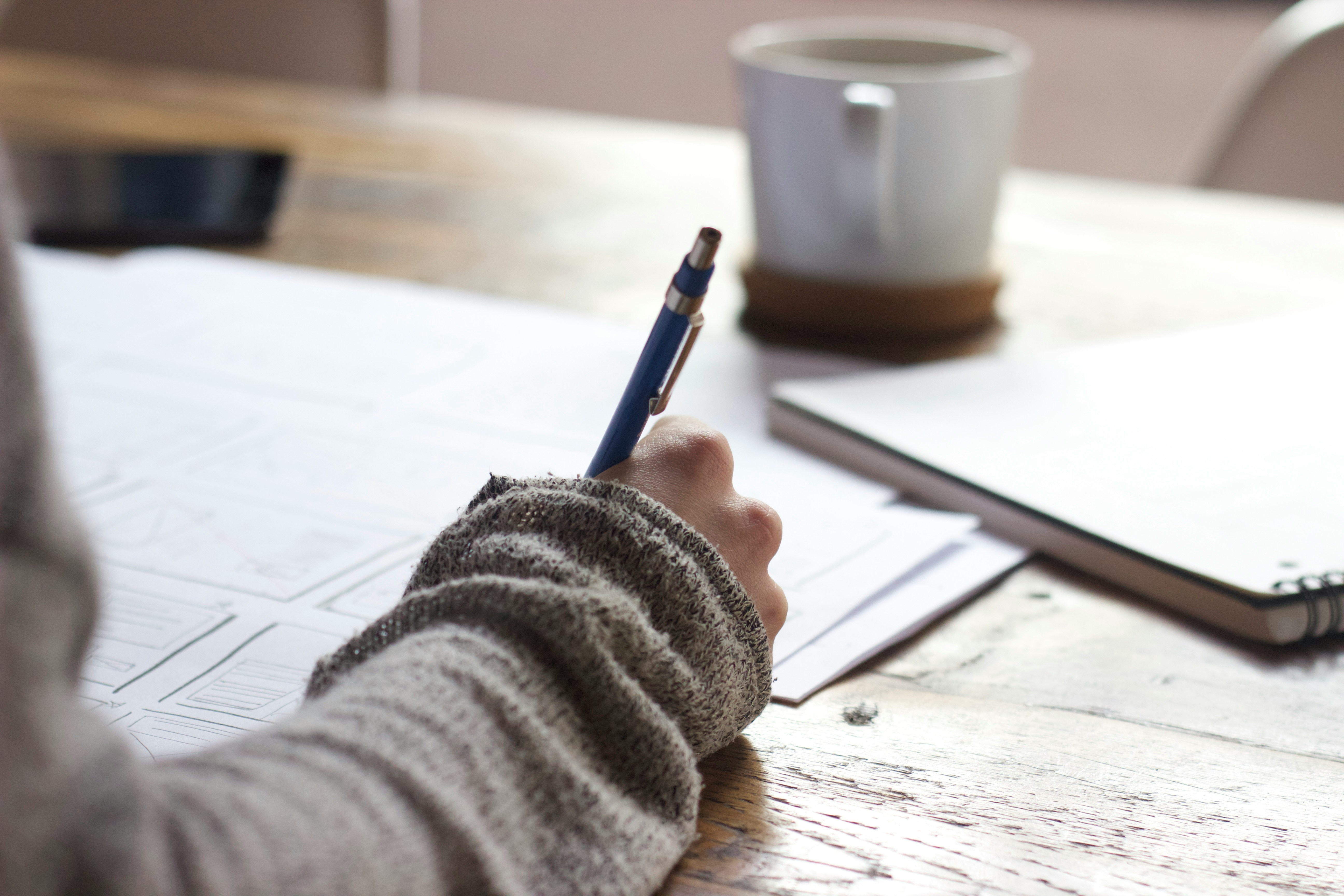 Wireframe sketching with pen on paper, mug on desk