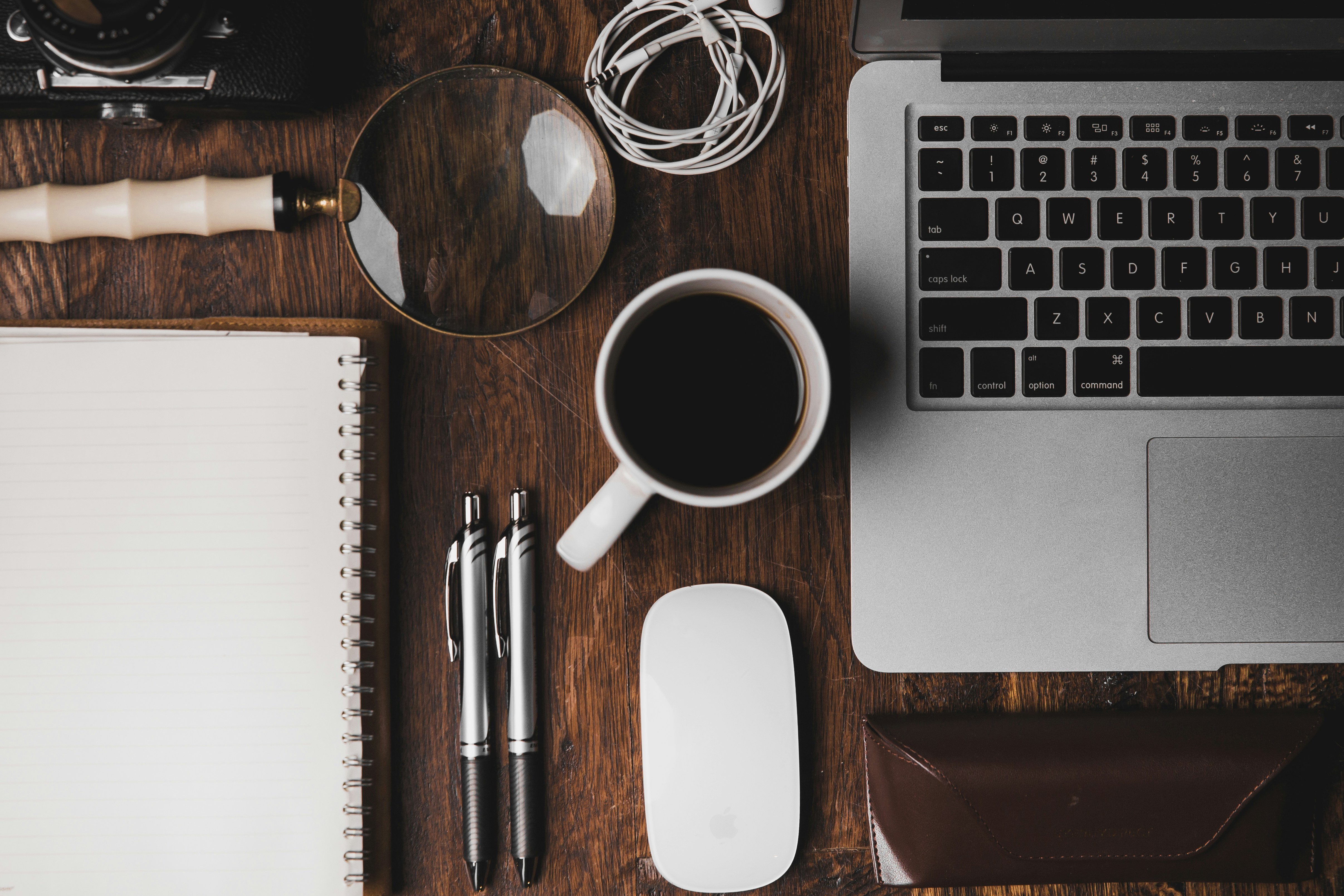 Workspace flatlay with MacBook, magnifying glass and Field Notes notebook
